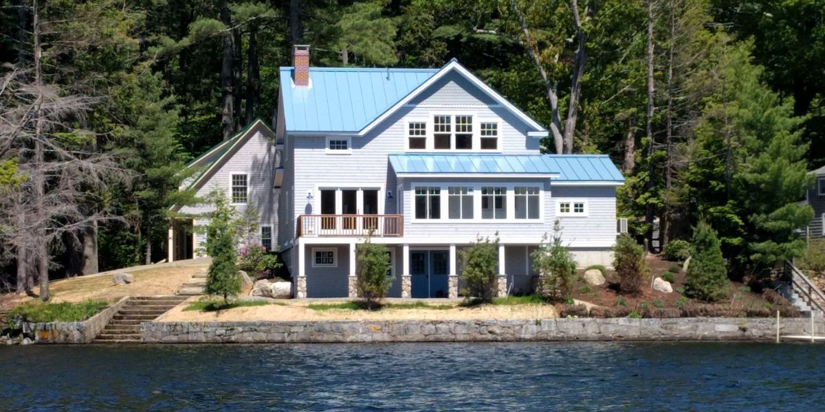 view from the water of new lakefront home in Camden, Maine with blue - gray roof and shingles.